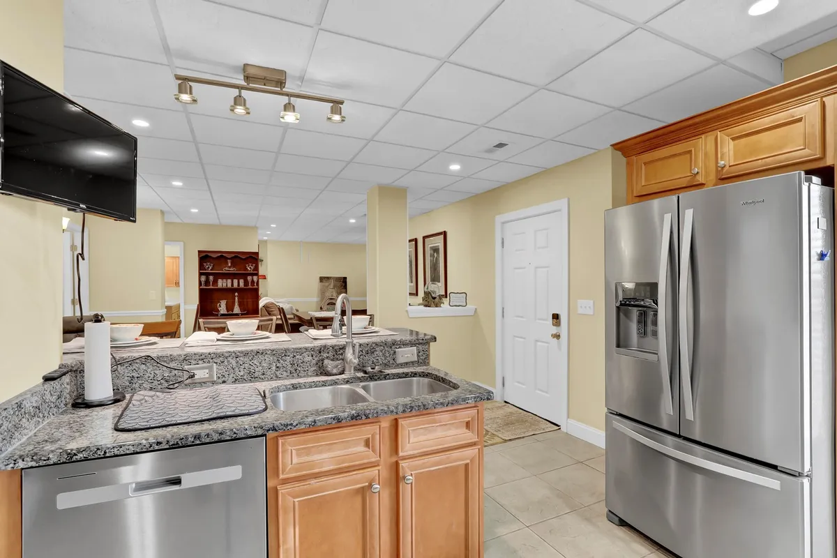 A welcoming kitchen scene featuring a granite countertop, stainless steel appliances, and a dining area in the background. The open layout encourages both cooking and social interactions, evoking scenes of family dinners and celebrations.