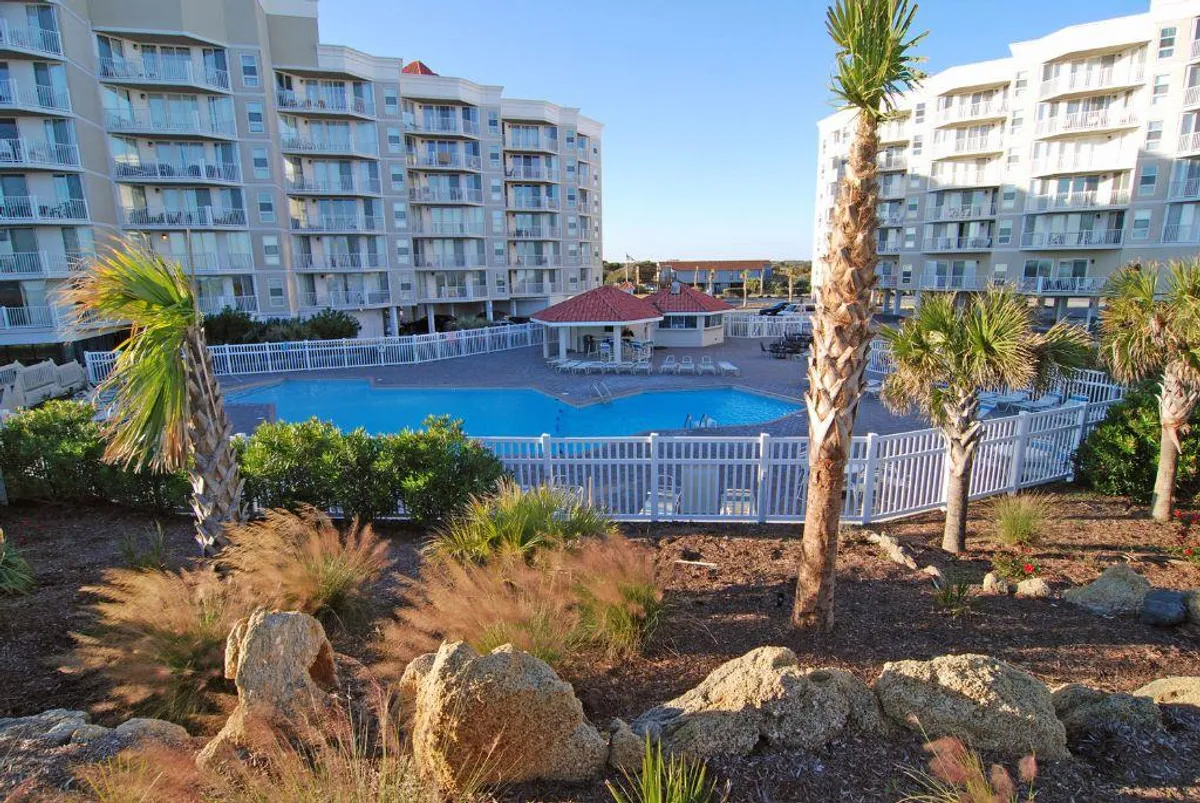 This exterior shot features a sparkling swimming pool surrounded by palm trees and a lounge area, with residential buildings visible in the background. The relaxed atmosphere highlights an inviting spot for swimming, sunbathing, and poolside socializing.